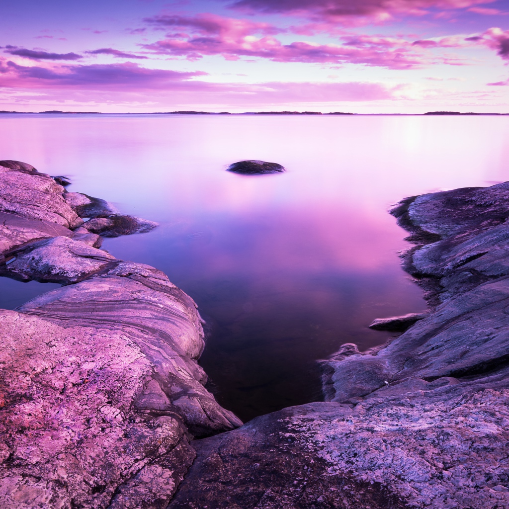 Lilac sunset in the sky over the water and stones