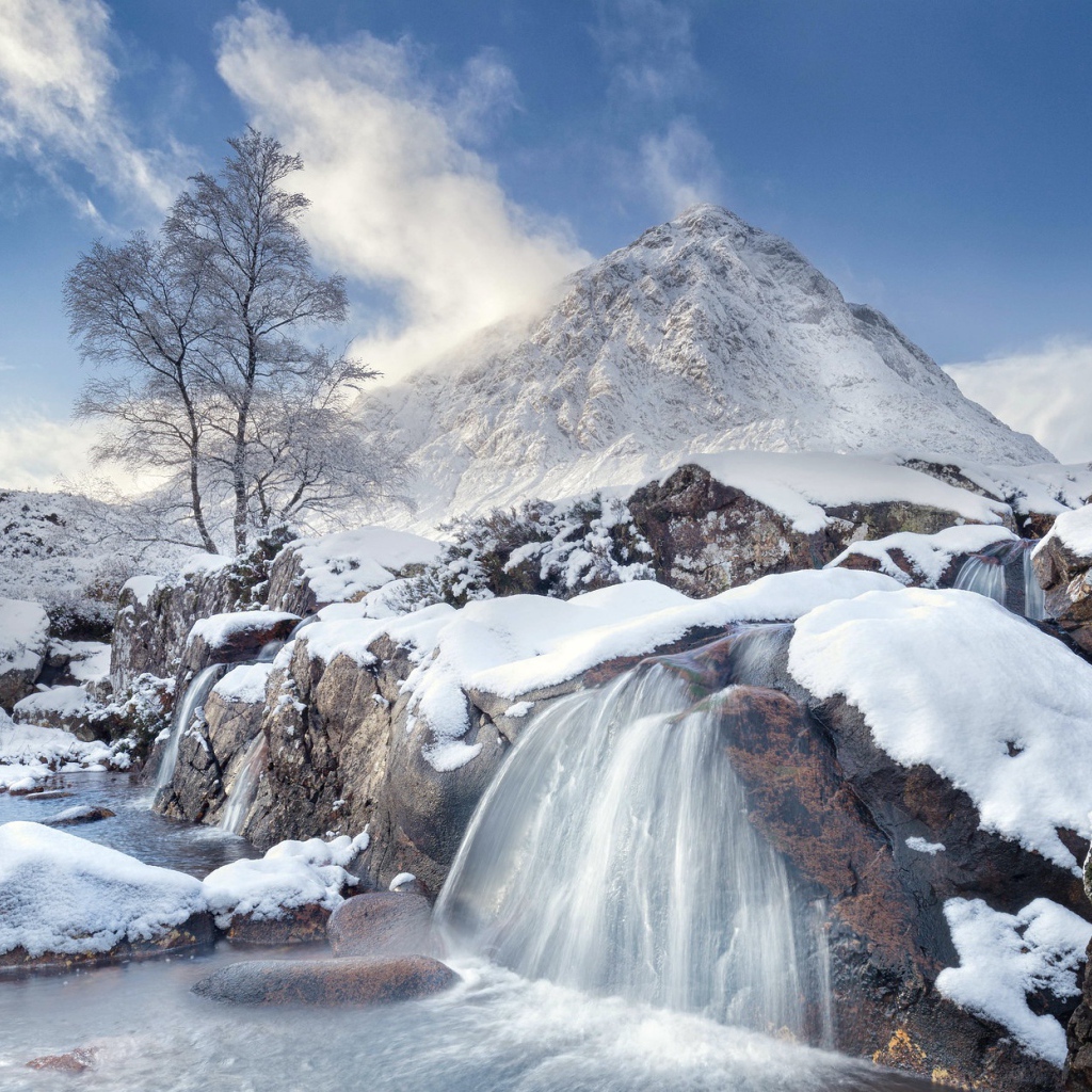 Водопад стекает с камней на фоне заснеженной горы