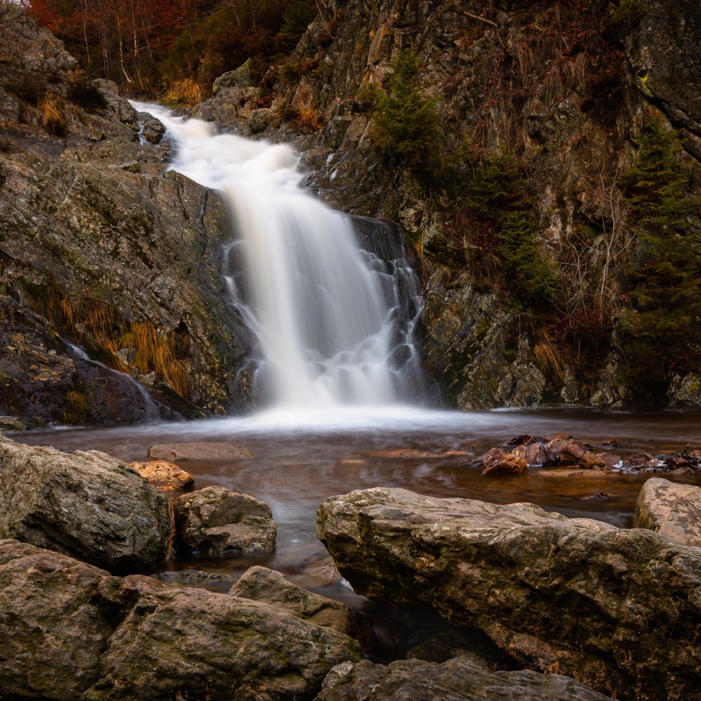 Быстрая вода водопада стекает по камням в горную реку