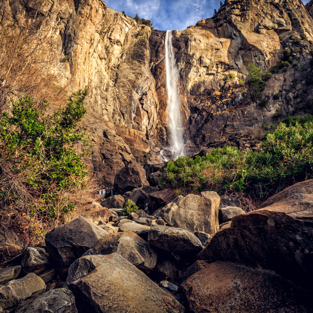 Водопад стекает с высокой скалы на камни 