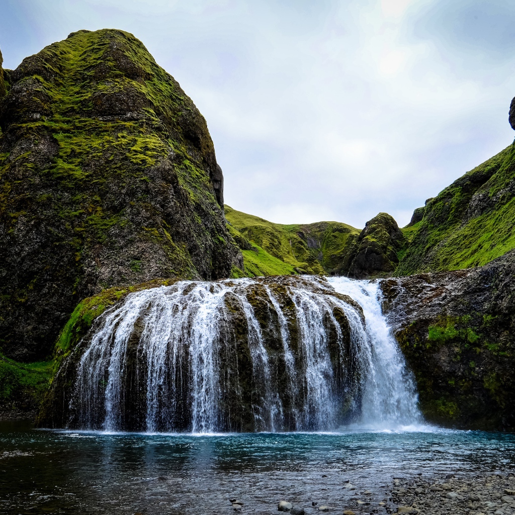 Белая вода водопада стекает по покрытым мхом скалам