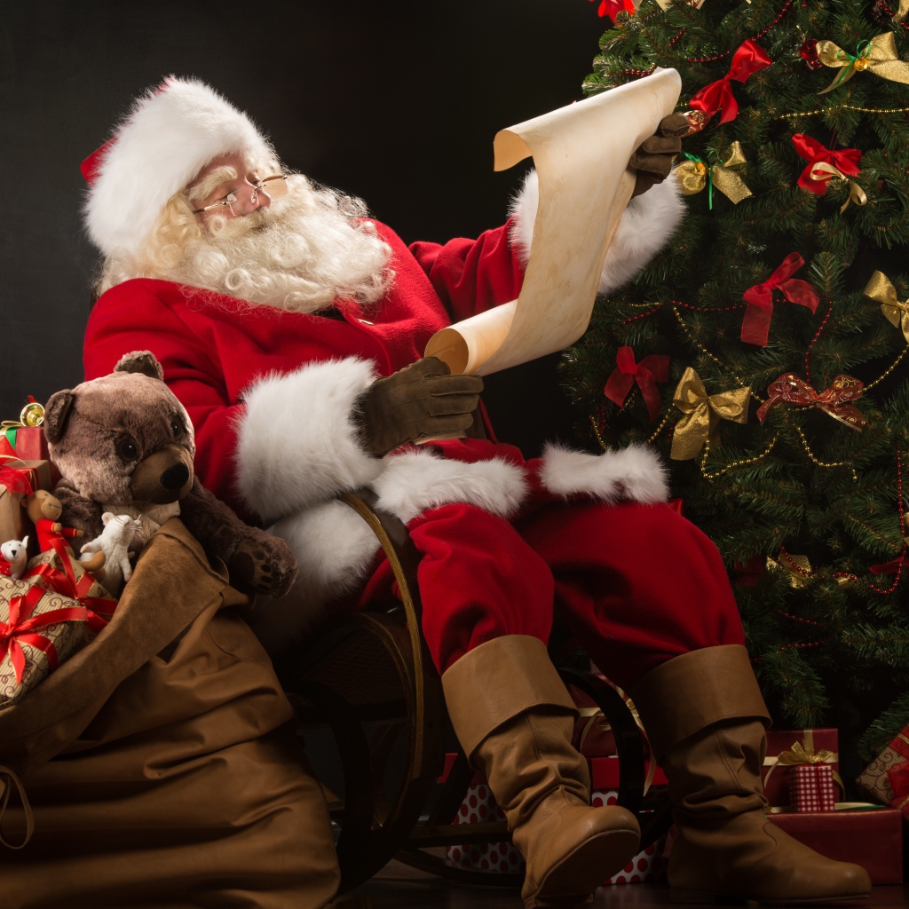 Санта Клаус с мешком подарков читает у елки