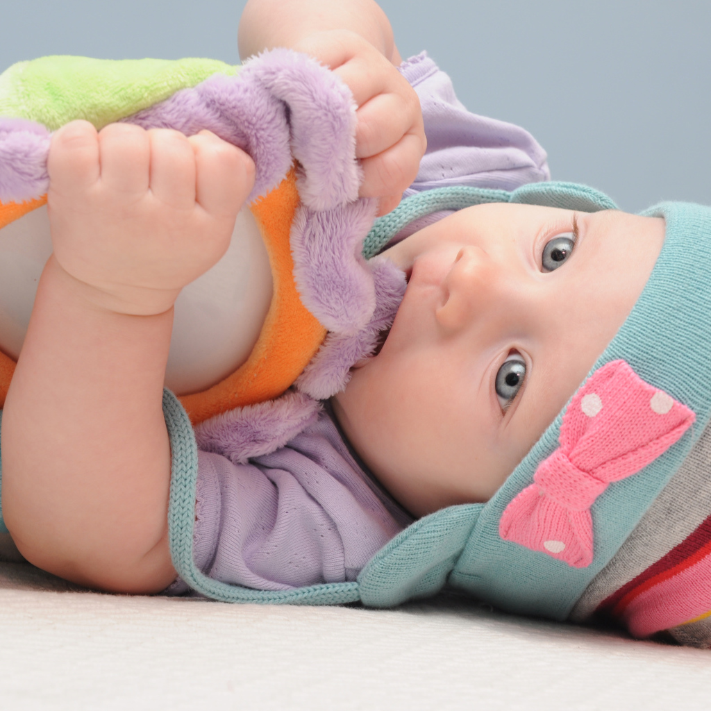 Младенец в шапке грызет мягкую игрушку