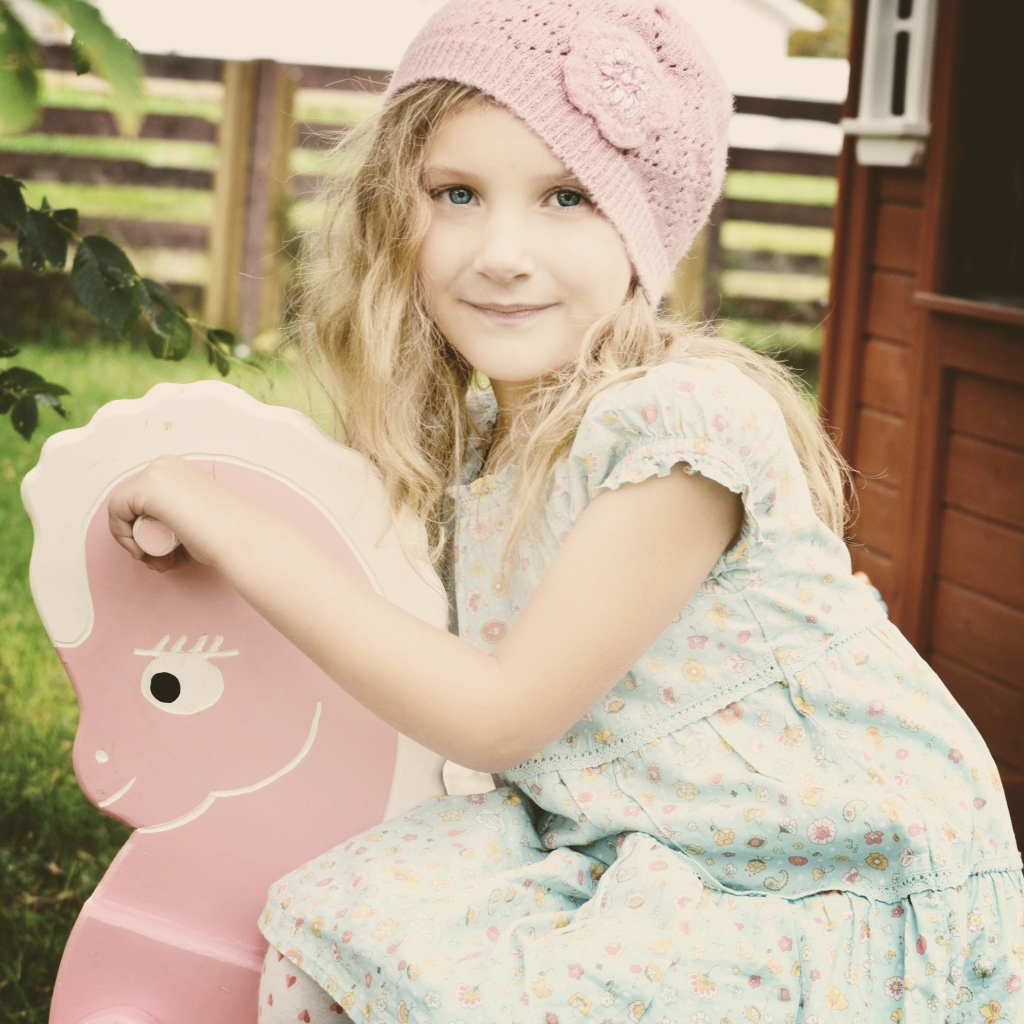 Девочка в платье сидит на деревянной лошади