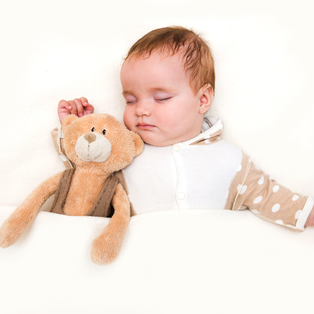 Грудной ребенок спит с плюшевым мишкой на белом фоне