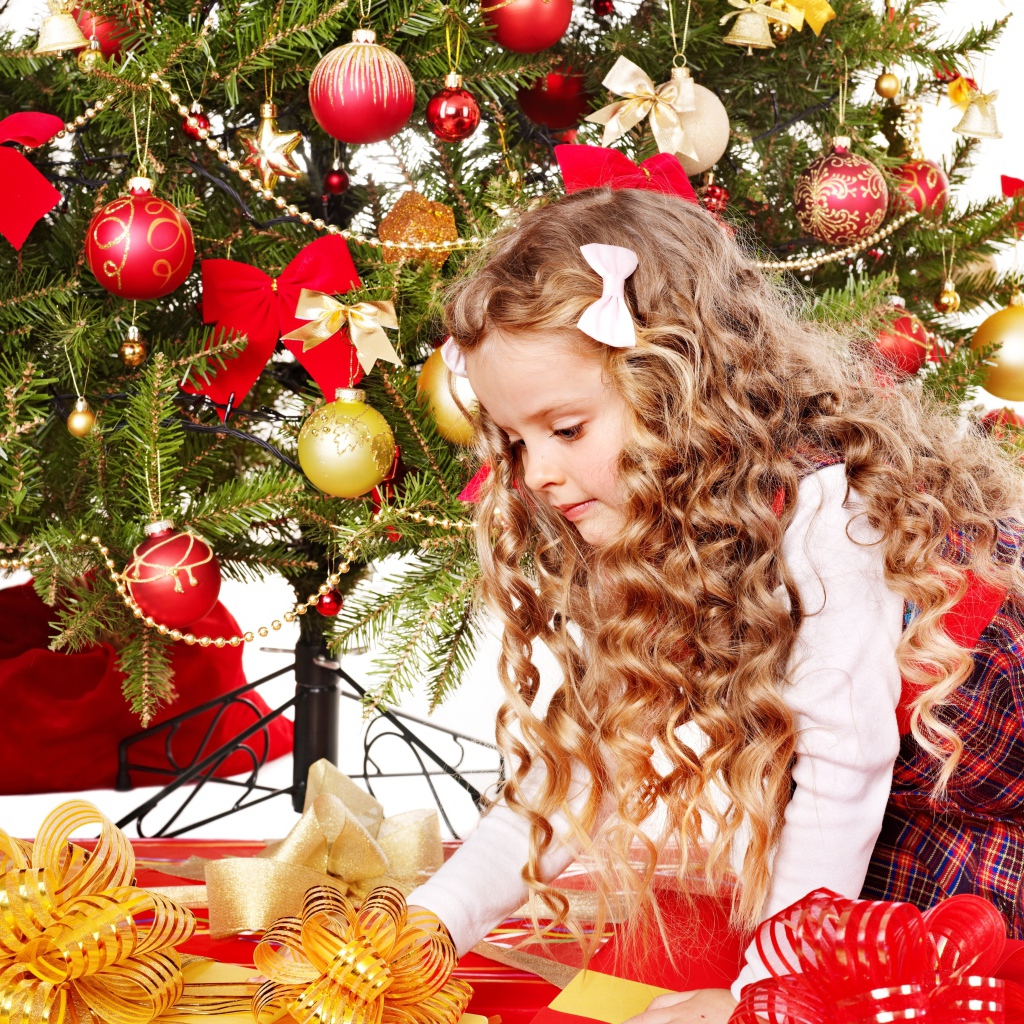 Красивая маленькая девочка смотрит подарки под елкой на новый год 