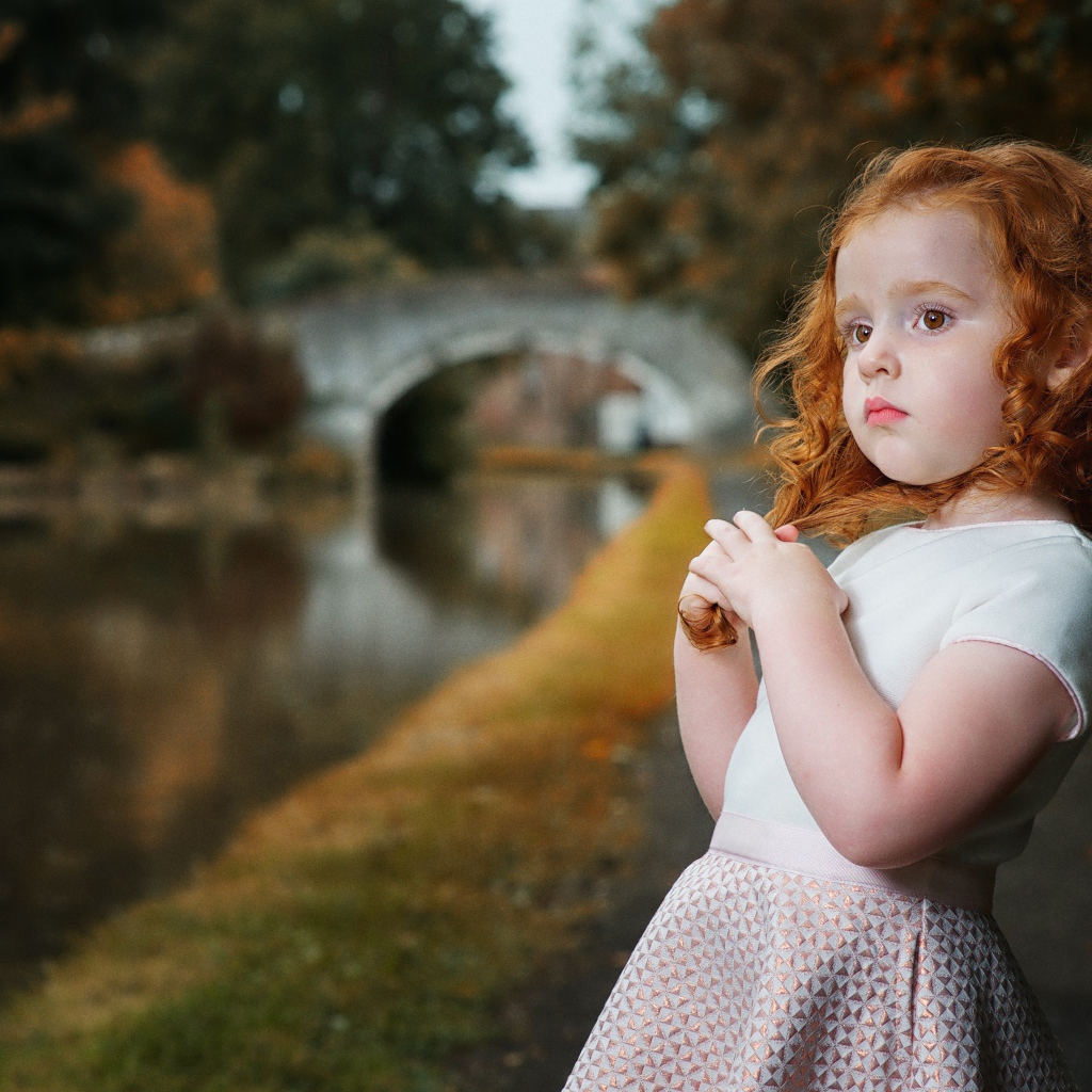 Красивая рыжеволосая девочка у реки в парке 