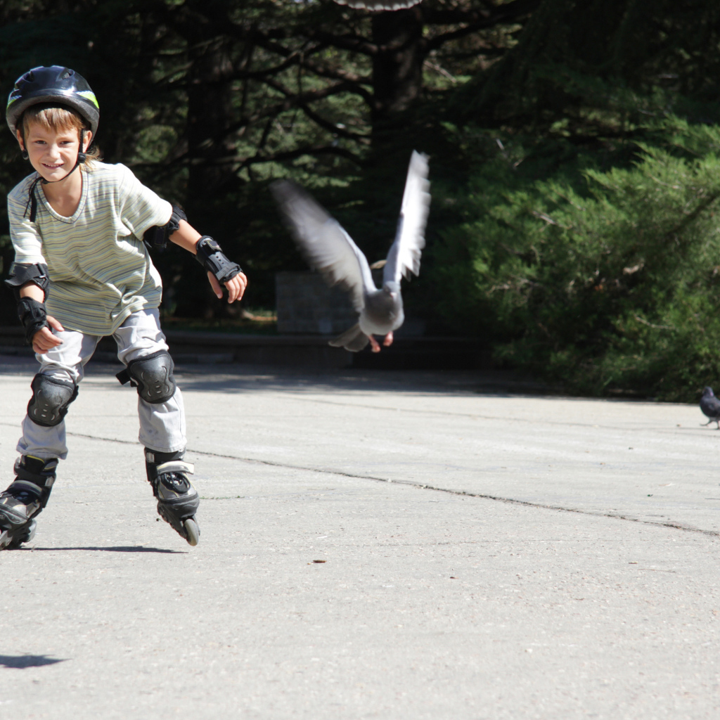 Мальчик катается на роликах на асфальте с голубями