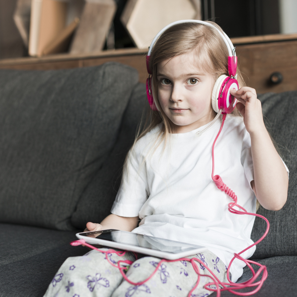 Девочка сидит на диване в наушниках  и с планшетом
