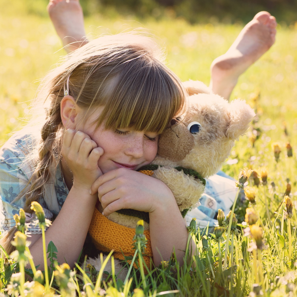 Девочка с игрушкой в руках лежит на траве 