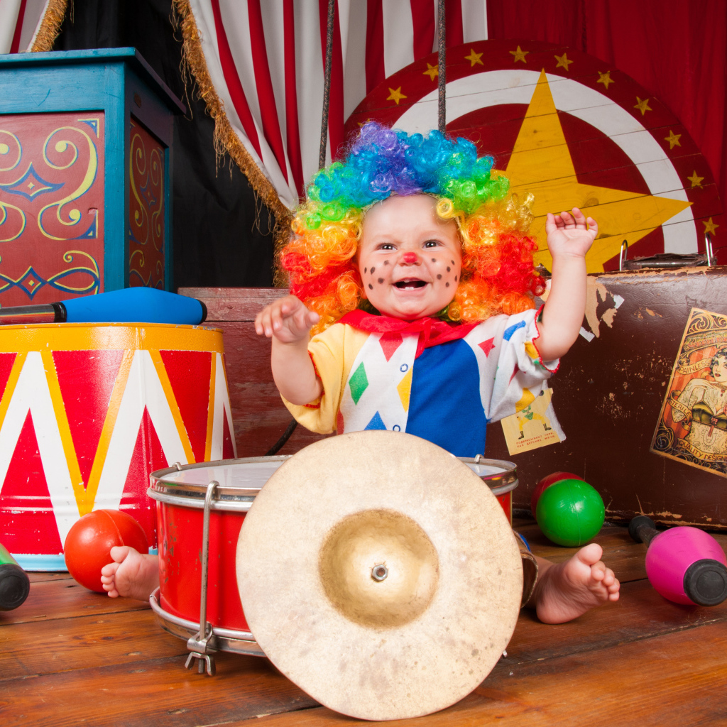 Маленький ребенок в костюме клоуна с музыкальными инструментами