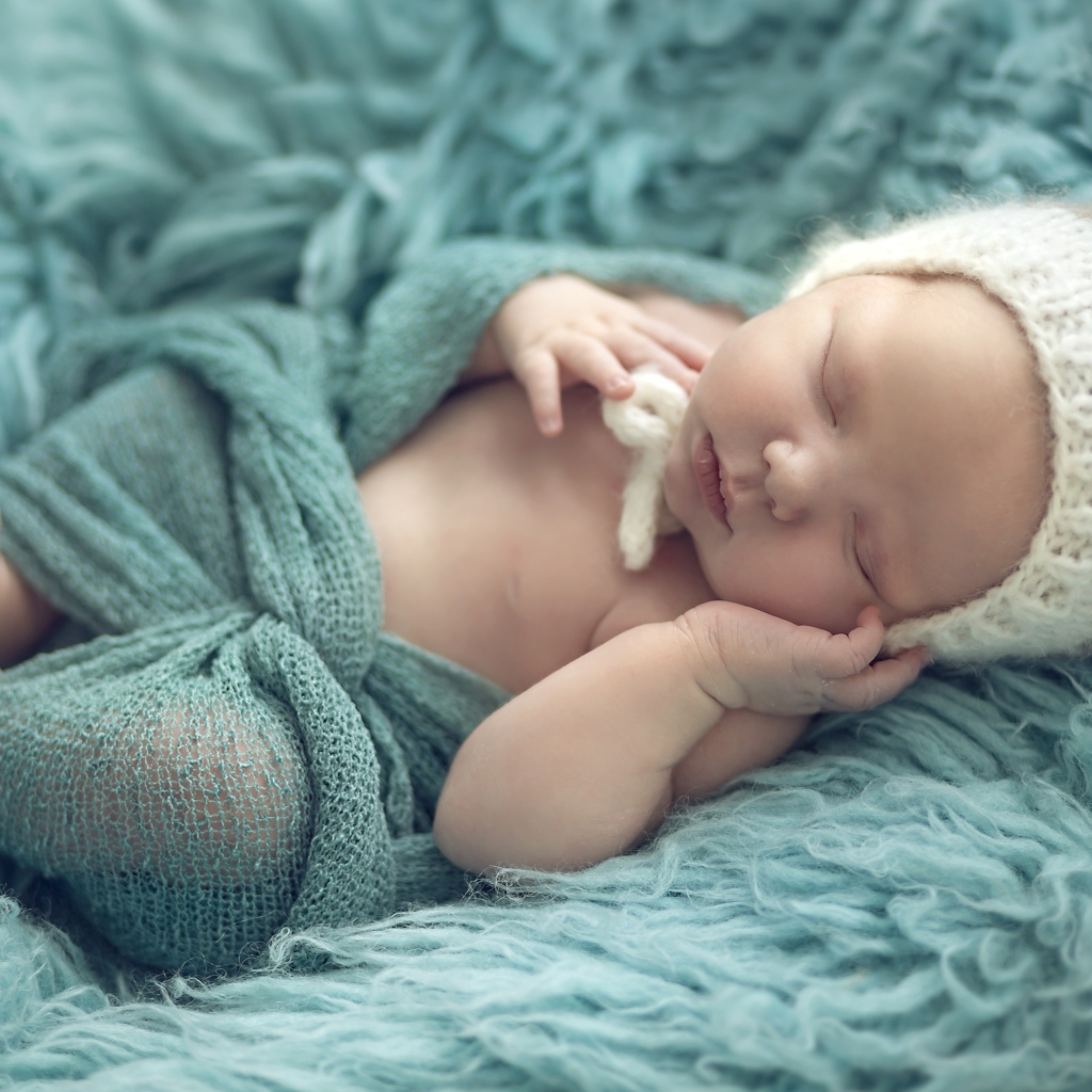 Маленький ребенок в вязаной шапке спит на меховом покрывале