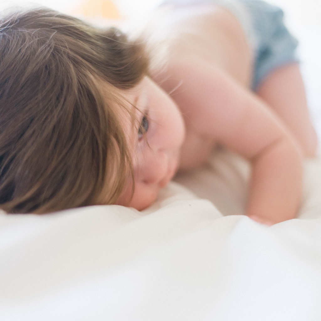 Маленький ребенок с русыми волосами лежит на кровати