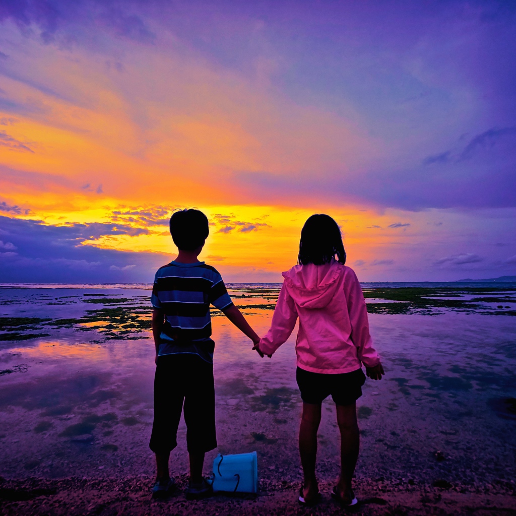 Маленькие мальчик и девочка стоят у воды на фоне заката 