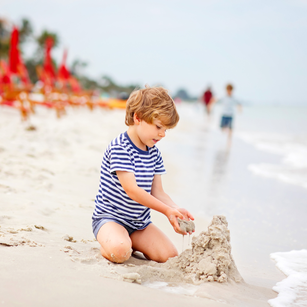 Маленький мальчик строит замок из песка на пляже