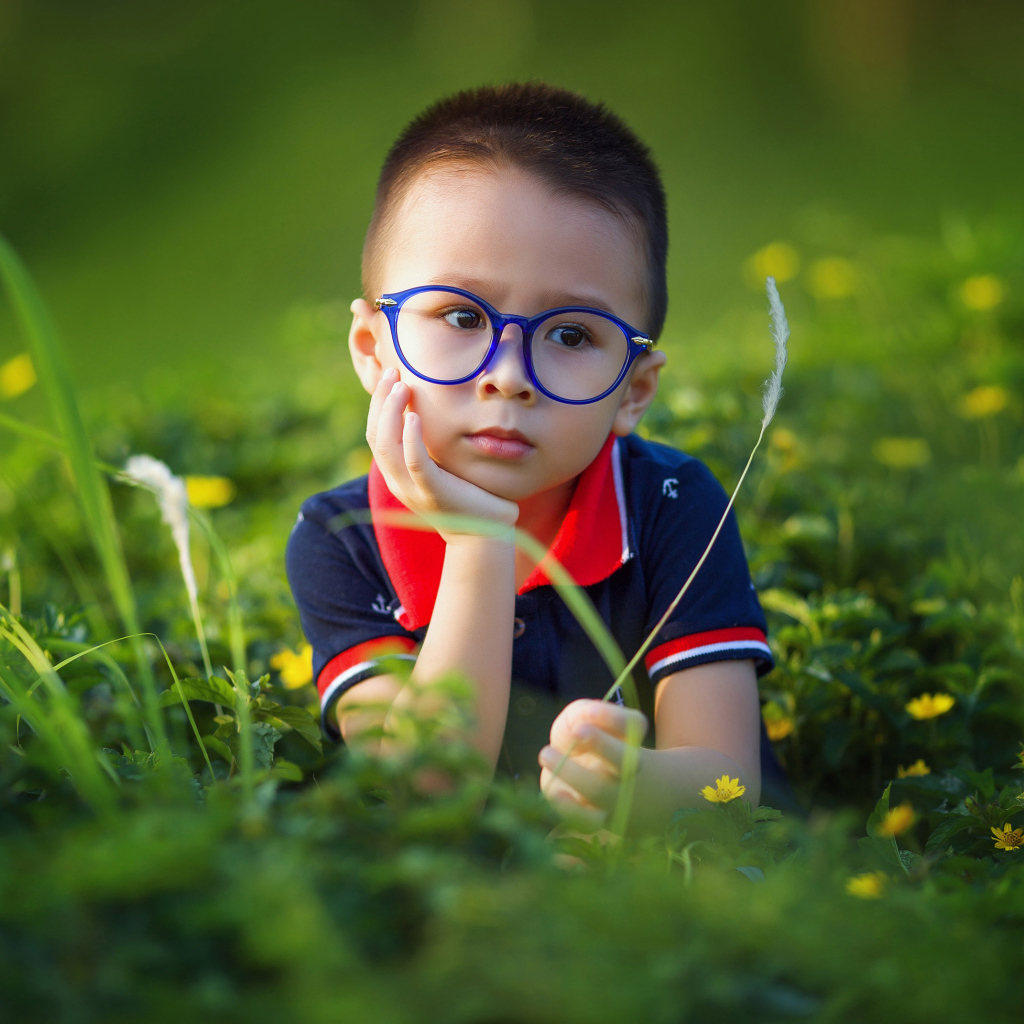 Маленький мальчик в очках лежит на зеленой траве