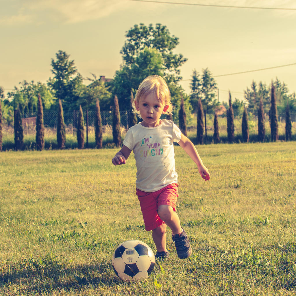 Маленький мальчик играет в футбол на зеленой траве