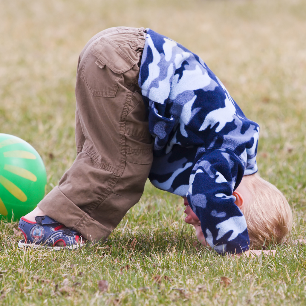 Маленький мальчик играет на траве с мячом