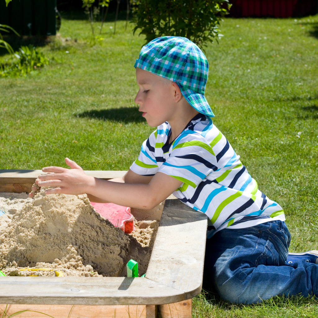 Маленький мальчик играет в песке на зеленой траве