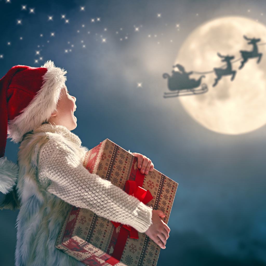 Маленький мальчик с подарком смотрит на улетающего Санта Клауса