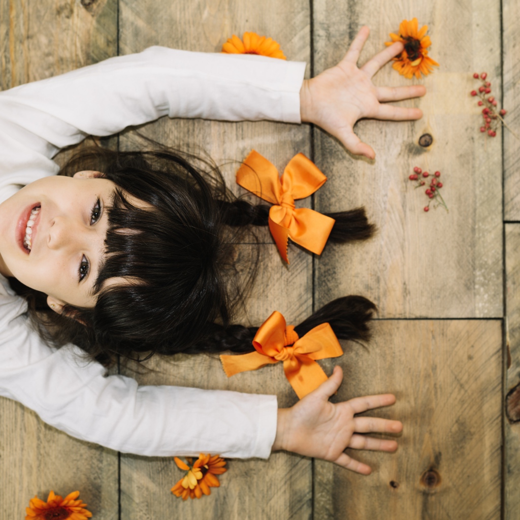 Маленькая веселая девочка с косичками лежит на полу