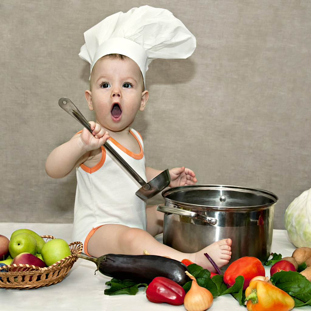 Маленький поваренок с кастрюлей на столе с овощами