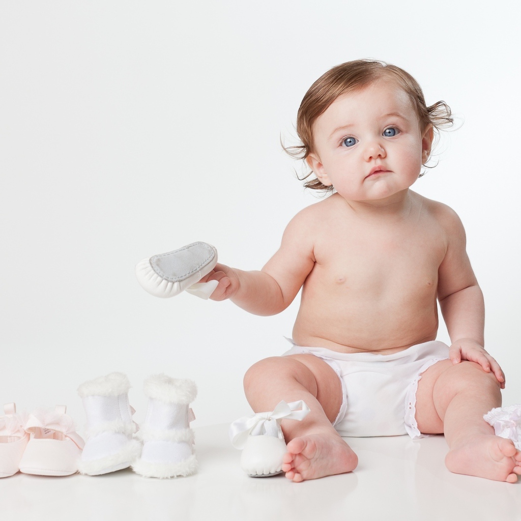 Маленький забавный голубоглазый малыш с обувью на белом фоне