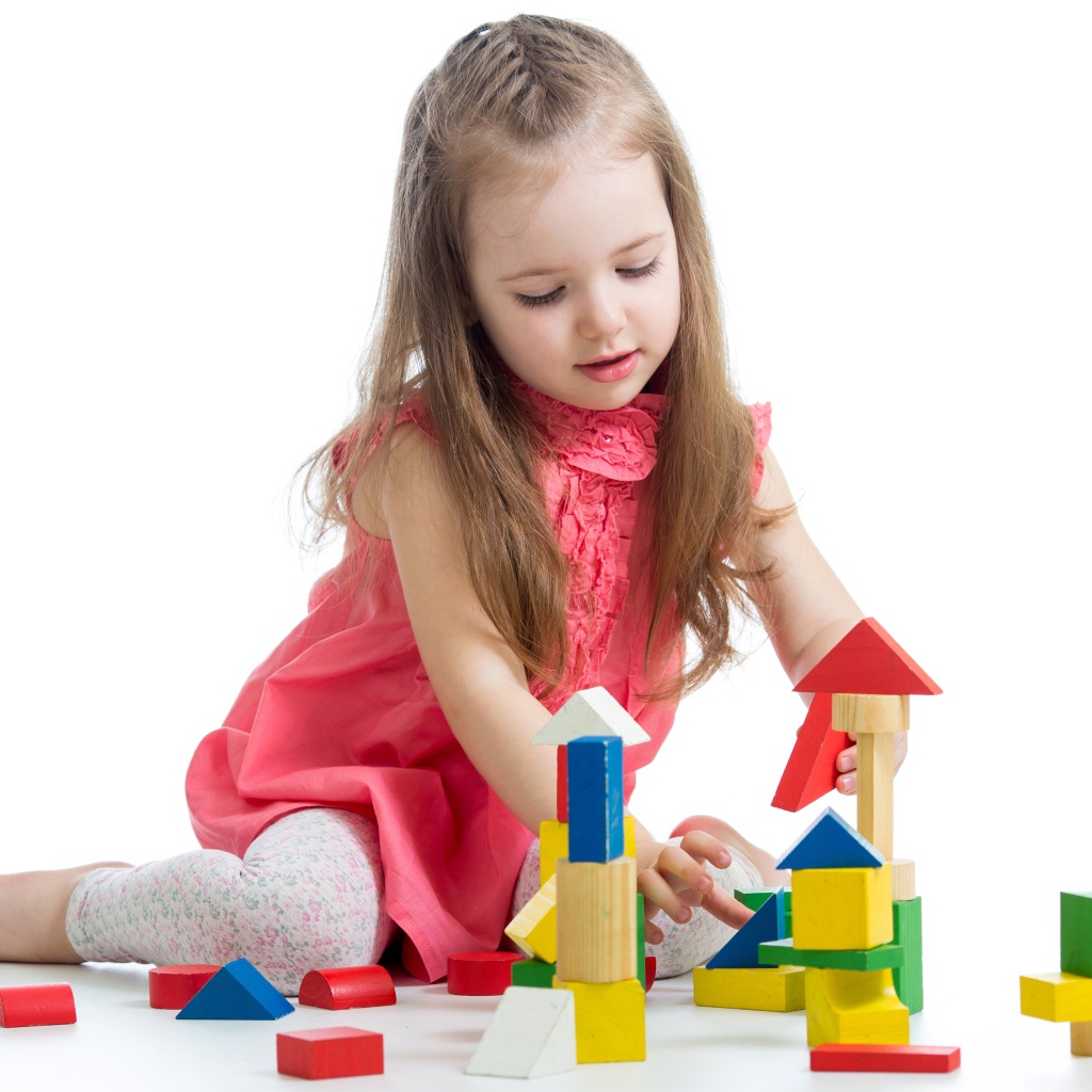 Маленькая девочка строит домик из кубиков на белом фоне