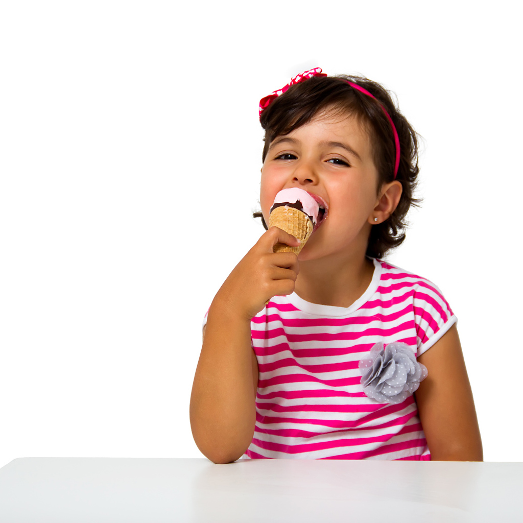 Маленькая девочка ест мороженое за столом на белом фоне