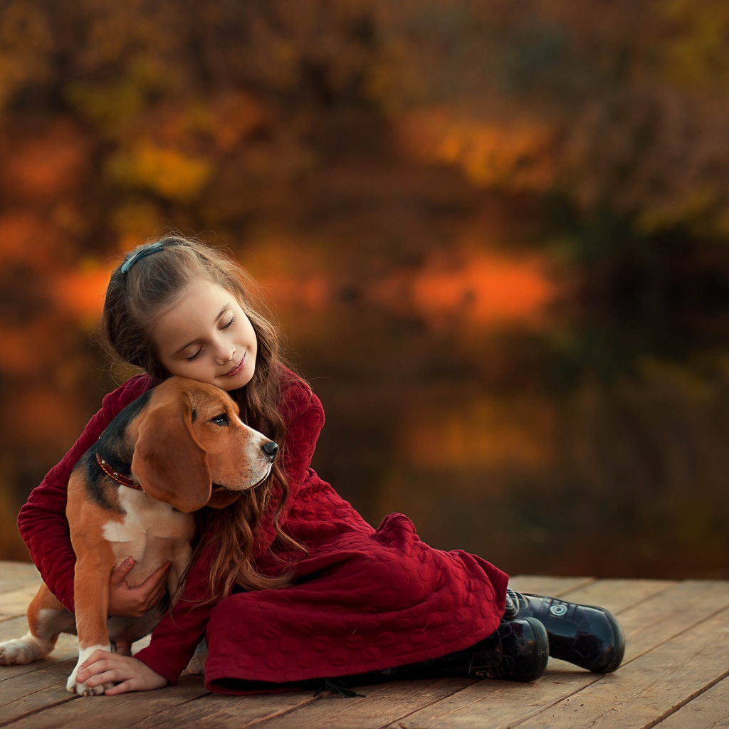 Маленькая девочка обнимает собаку породы бигль на мосту