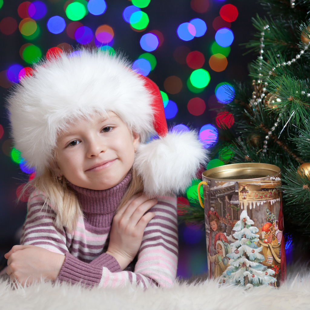 Маленькая девочка в новогодней шапке у елки