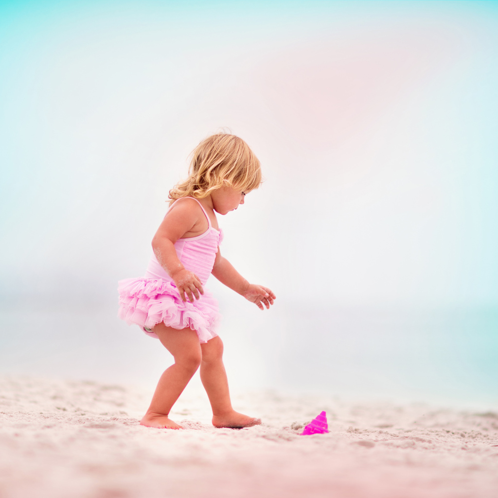 Маленькая девочка в розовом купальнике на песке