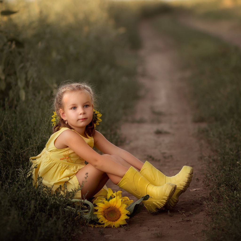 Маленькая девочка в желтом платье сидит на земле с подсолнухами