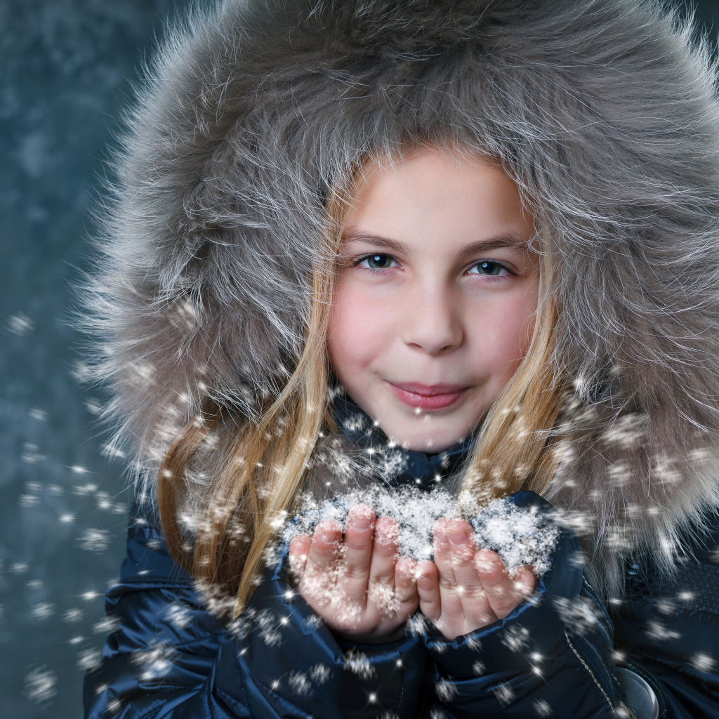 Маленькая девочка в капюшоне сдувает снежинки с ладоней