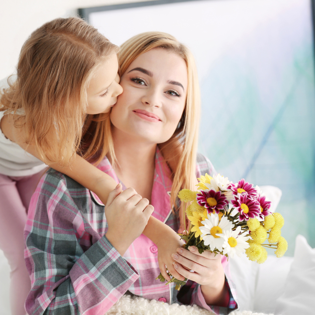 Маленькая девочка целует маму с букетом