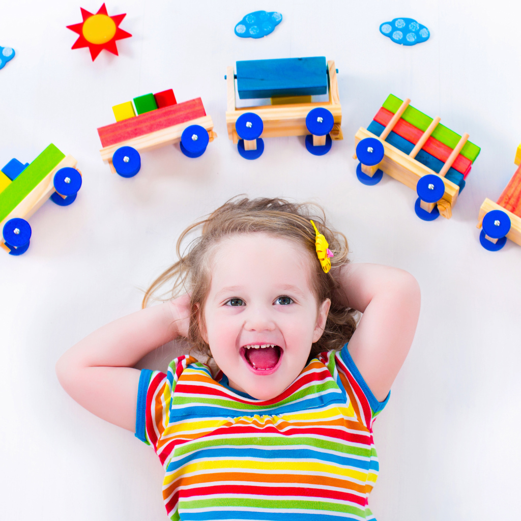 Маленькая девочка на сером фоне с игрушечным паровозом 