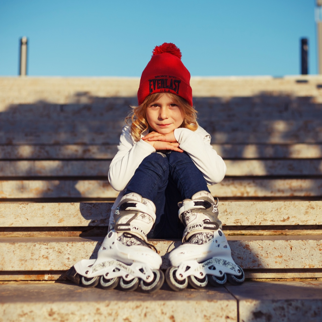 Маленькая девочка в роликах сидит на ступеньках 