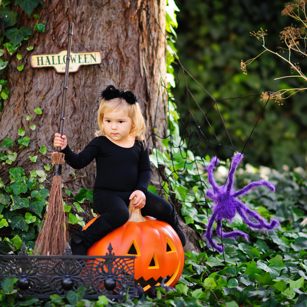 Маленькая девочка сидит на тыкве в лесу в костюме на Хэллоуин 