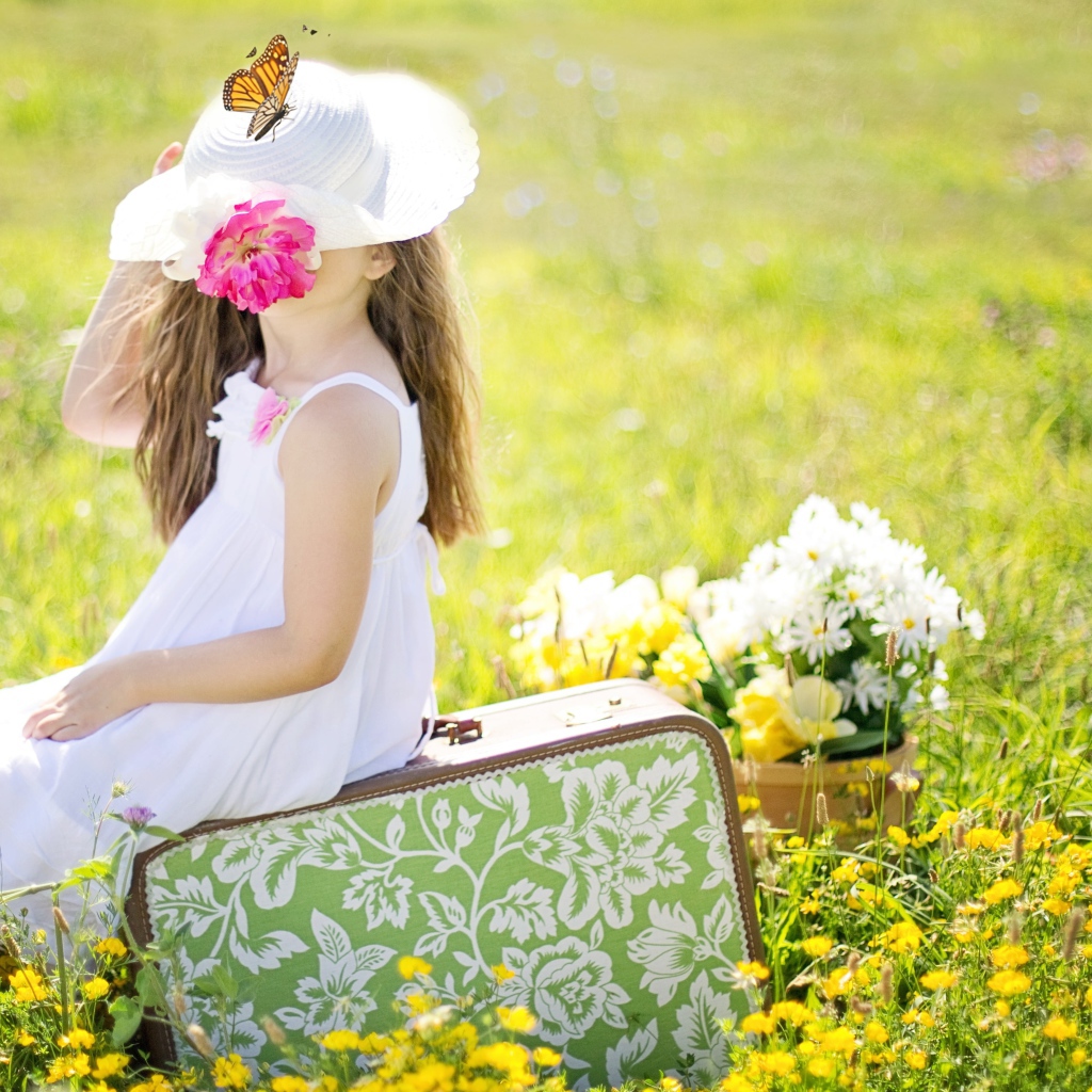 Маленькая девочка сидит на чемодане на поле с цветами