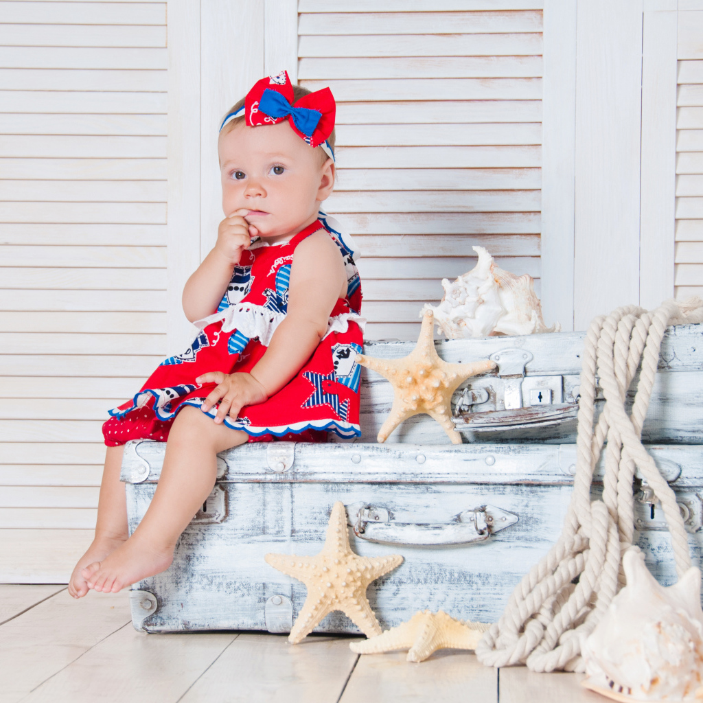 Маленькая девочка сидит на чемодане с морскими звездами