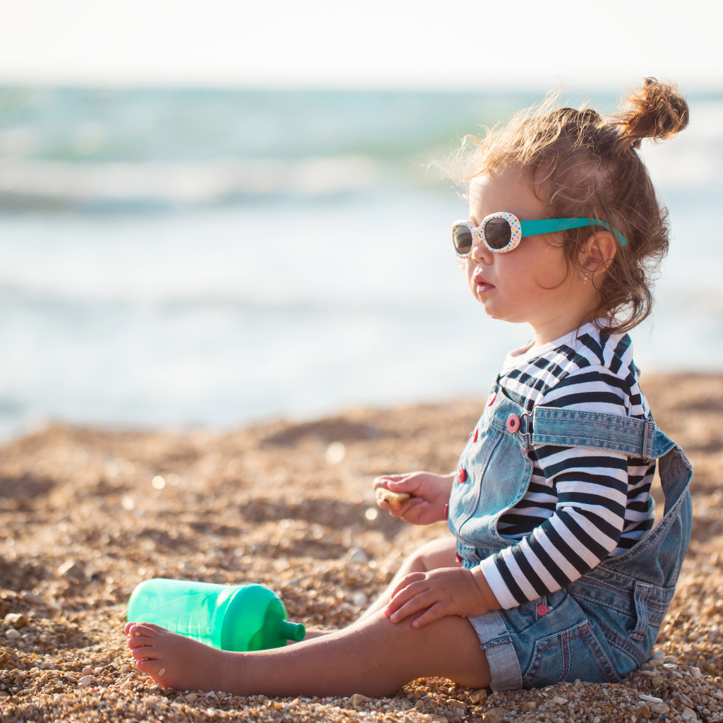Маленькая девочка сидит на песке на пляже