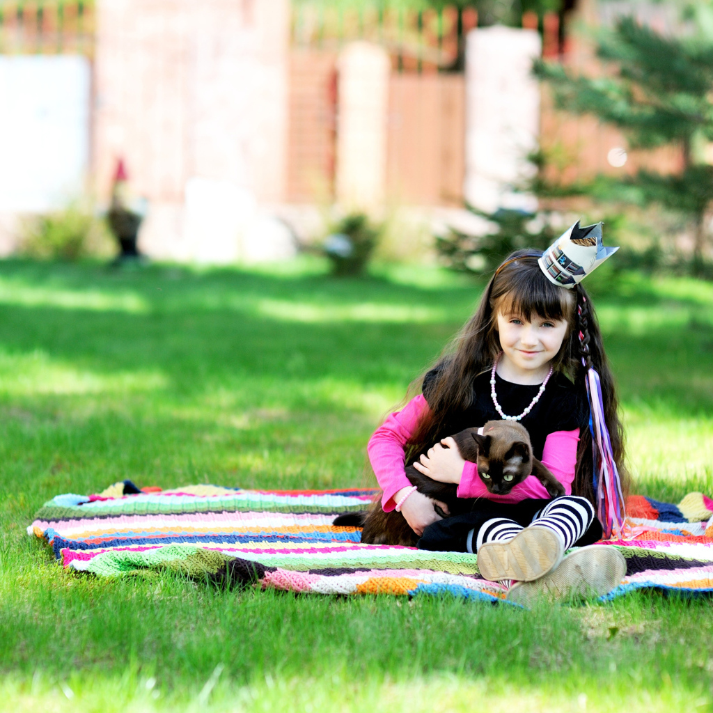 Маленькая девочка с котом сидит на зеленой траве