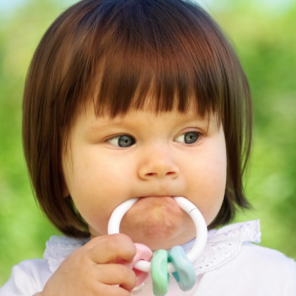 Маленькая девочка с погремушкой во рту