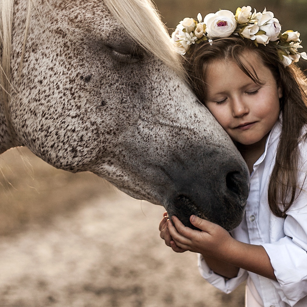 Маленькая девочка с венком на голове обнимает лошадь