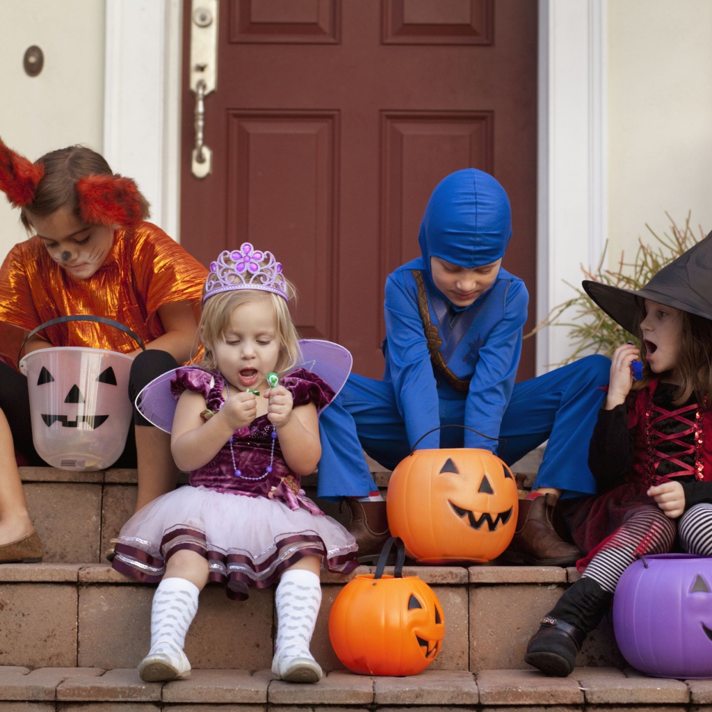 Маленькие дети в костюмах на Хэллоуин сидят на ступеньках со сладостями