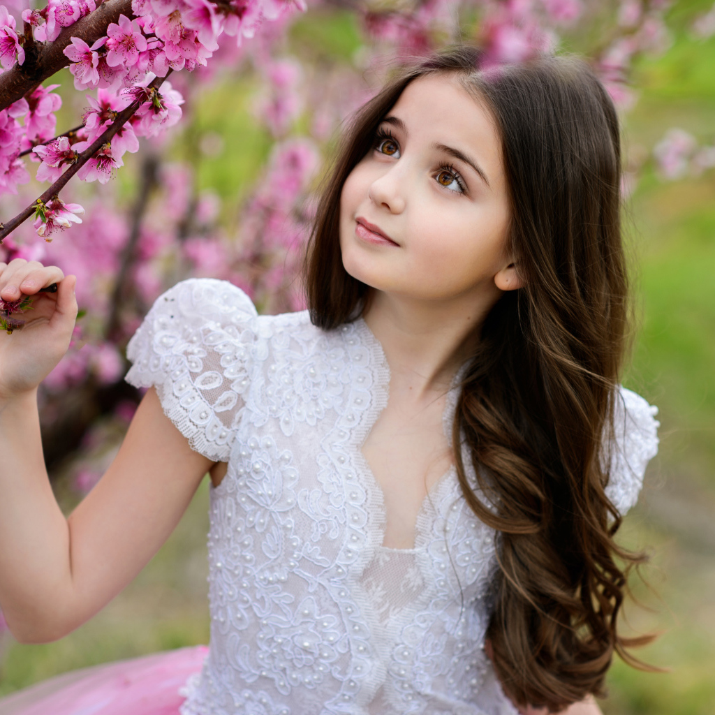 Маленькая длинноволосая девочка у дерева с розовыми цветами