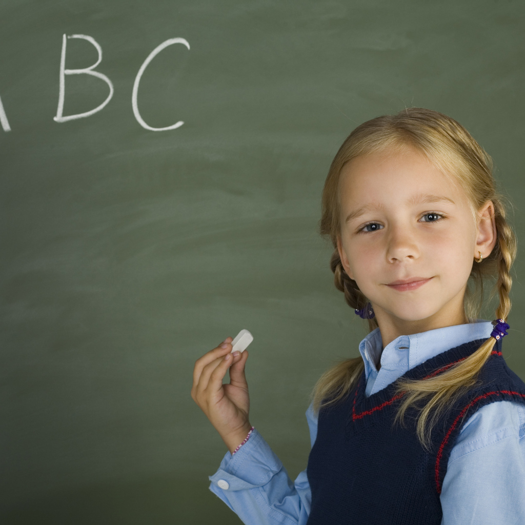 Маленькая школьница пишет буквы на доске 