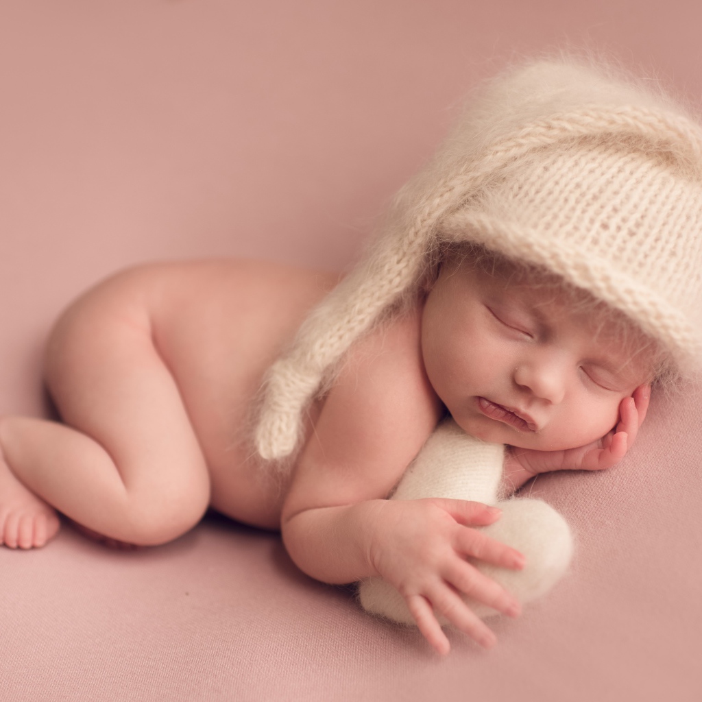 Маленький спящий ребенок в теплой шапке на розовом фоне
