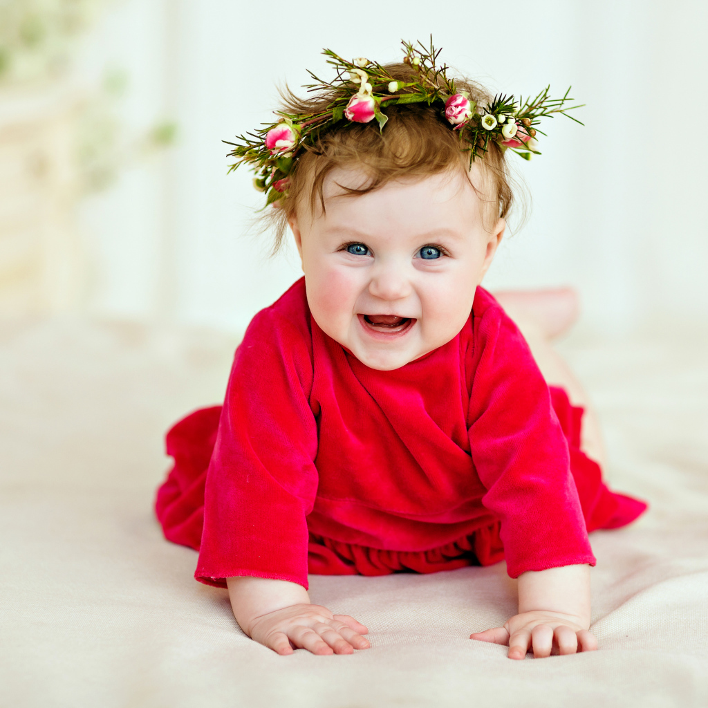 Маленькая улыбающаяся девочка в красном платье с венком на голове