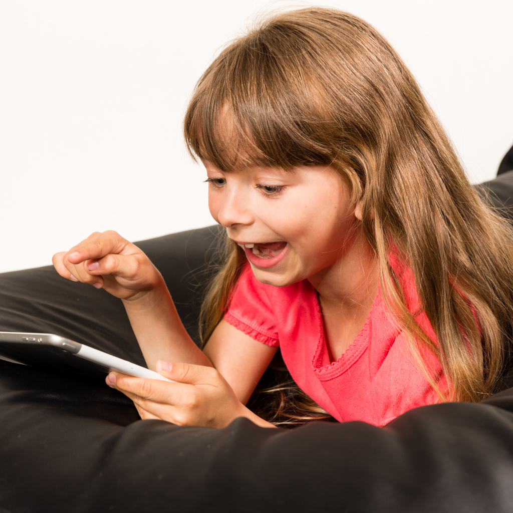 Маленькая улыбающаяся девочка лежит с планшетом